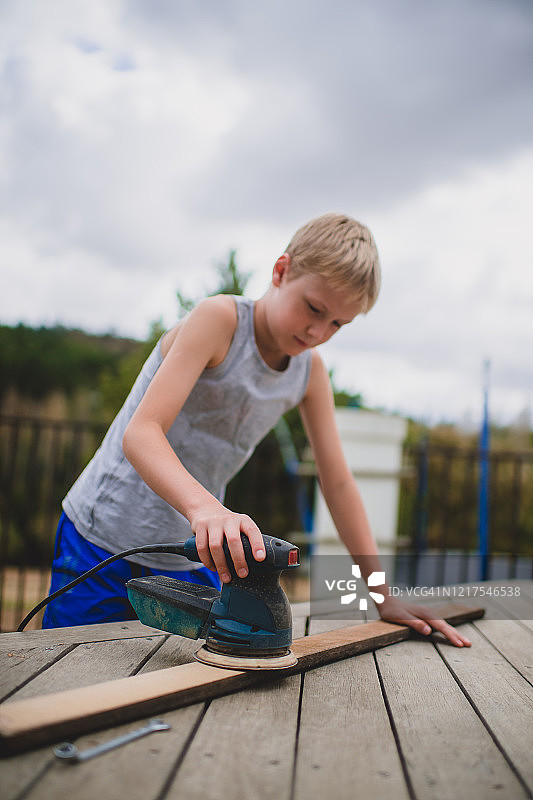 男孩用电动砂光机打磨木板图片素材