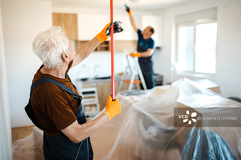 辛勤工作的年长工人在客户公寓里粉刷天花板图片素材