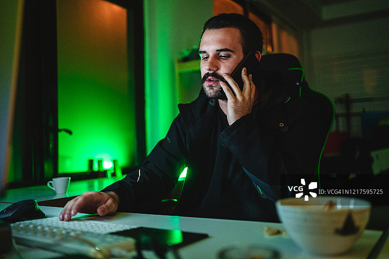 男子晚上在电脑前工作，用手机通话图片素材