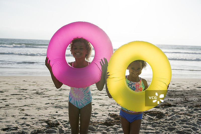 可爱的姐妹俩在沙滩上玩充气泳圈图片素材