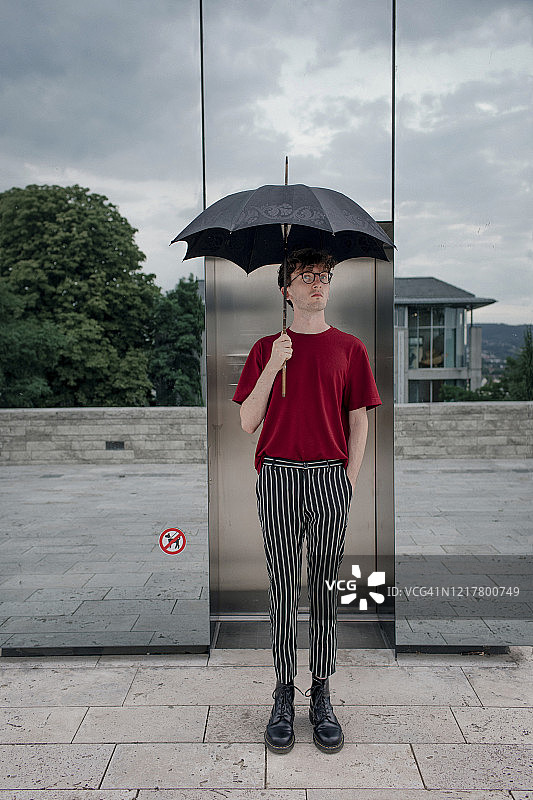 德国卡塞尔，手持雨伞的严肃青年男子肖像图片素材