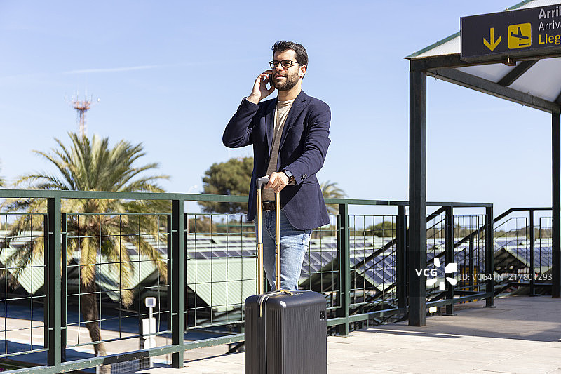 在机场屋顶露台上拉着行李箱打电话的商人图片素材