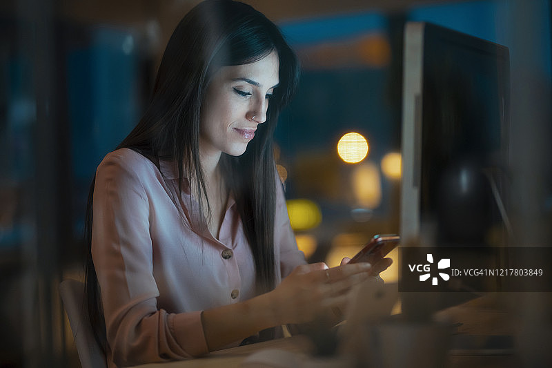 年轻女人坐在办公室的桌旁看智能手机图片素材