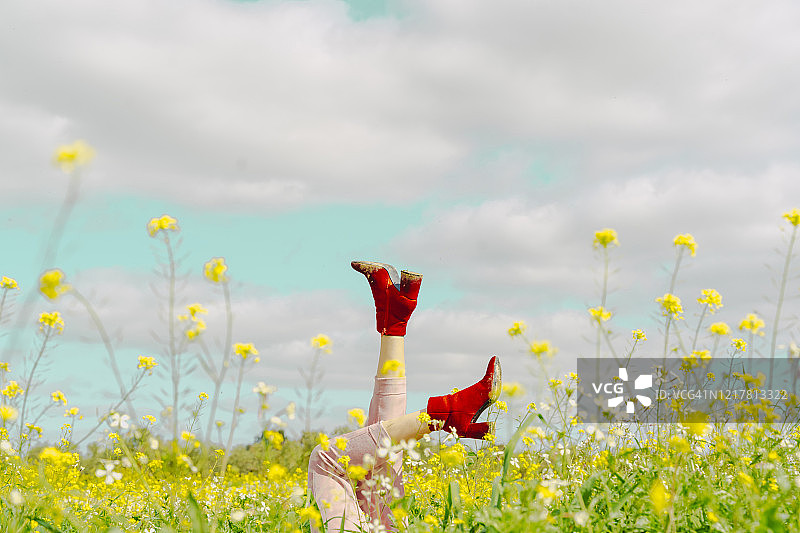 穿着红色踝靴的女人躺在春天花丛中的腿图片素材