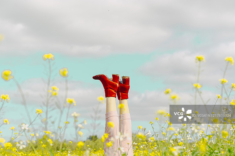 穿着红色踝靴的女人躺在春天花丛中的腿图片素材