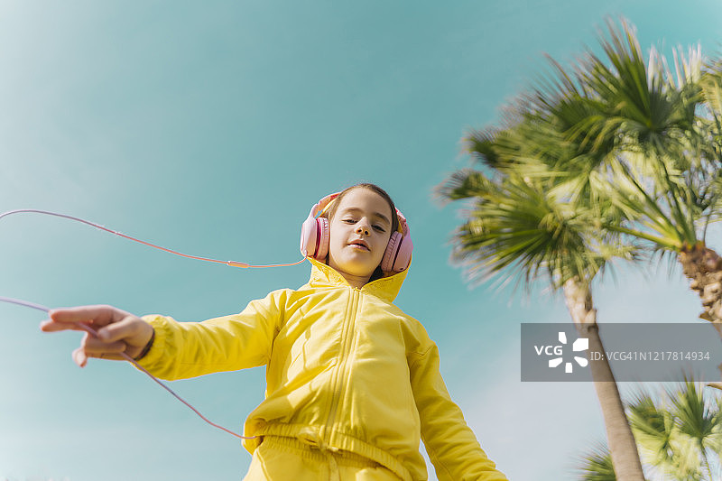 戴着黄色连帽夹克、用耳机听音乐的小女孩肖像图片素材