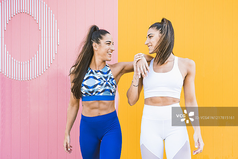 微笑的运动双胞胎在黄色和粉红色墙壁前摆姿势图片素材