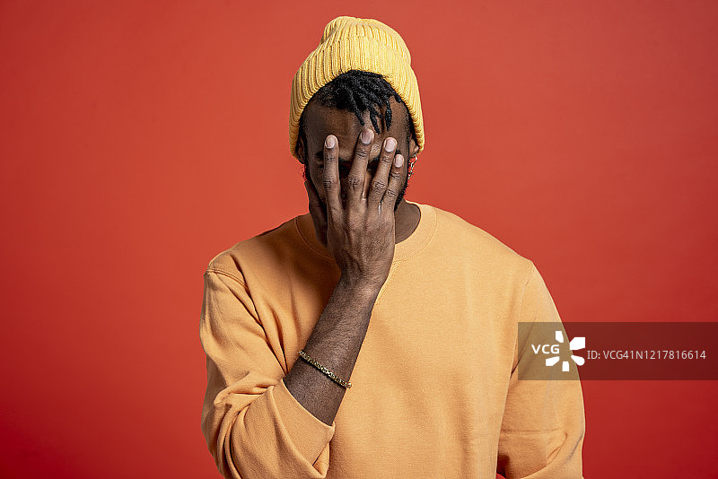 在橙色墙壁前捂住脸的年轻男人图片素材