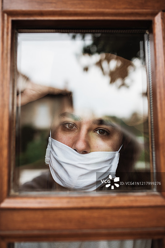 隔离期间戴着口罩望向窗外的年轻男人图片素材
