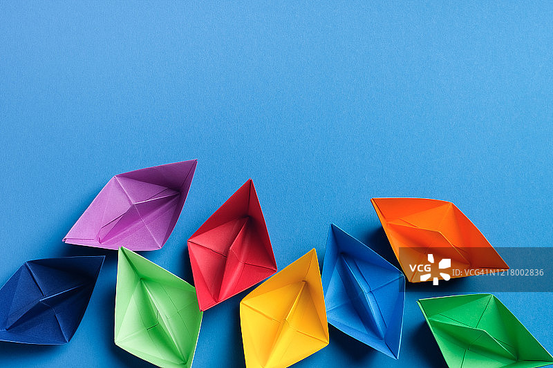明亮蓝色背景上的彩色纸船，留白区域图片素材