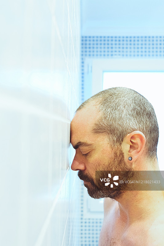 男子头靠在浴室墙上图片素材