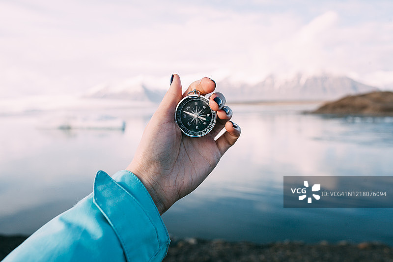冬季傍晚，年轻女子在冰岛冰川泻湖前手持指南针图片素材