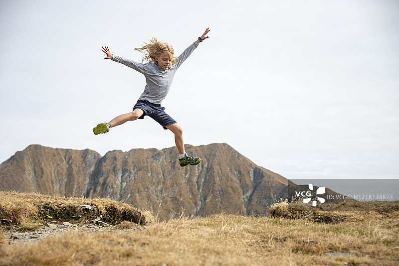 可爱的小男孩跳到山顶上，背景是摩尔多瓦努峰和维斯特亚峰，罗马尼亚法格拉什山图片素材