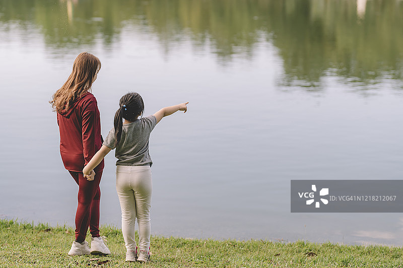 中国母亲早上在房子前和女儿在湖边指点（后视图）图片素材
