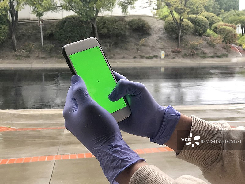戴手套的手拿着带有绿色屏幕的手机图片素材
