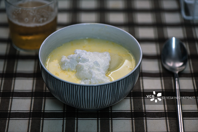 一碗黄色汤，配土豆和鸡蛋，桌上有一把勺子和一杯啤酒图片素材