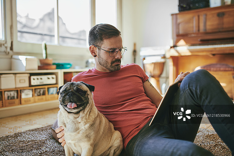 30多岁的男人在公寓地板上靠着平板电脑和狗图片素材