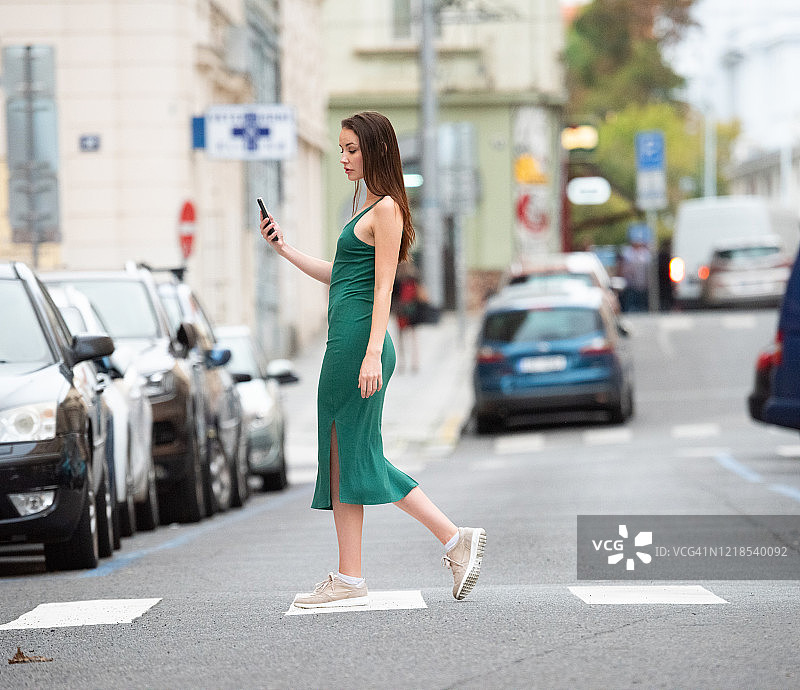 穿绿色连衣裙的女人过马路时使用手机图片素材