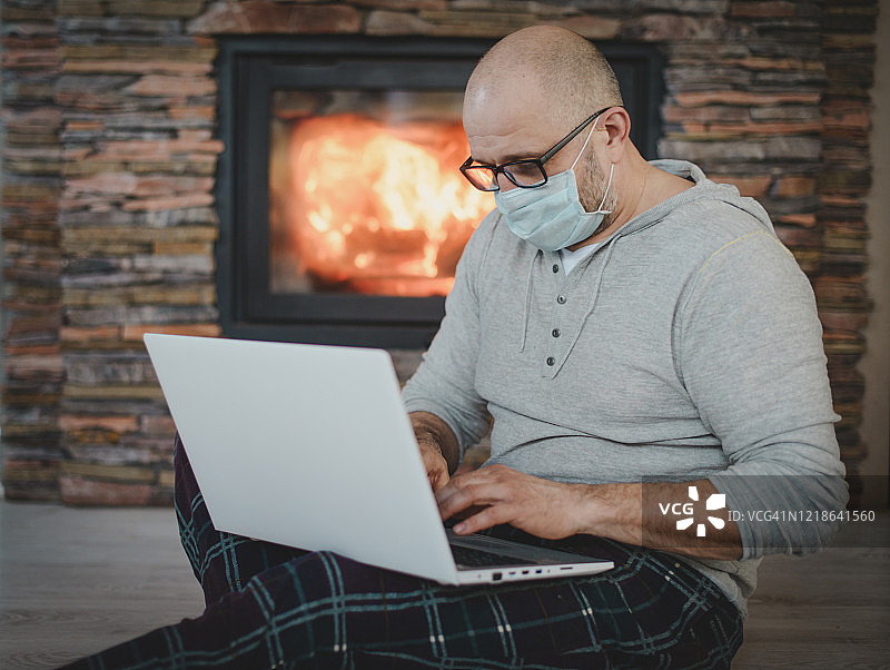 中年男子戴着口罩在家工作，使用笔记本电脑（壁炉）图片素材