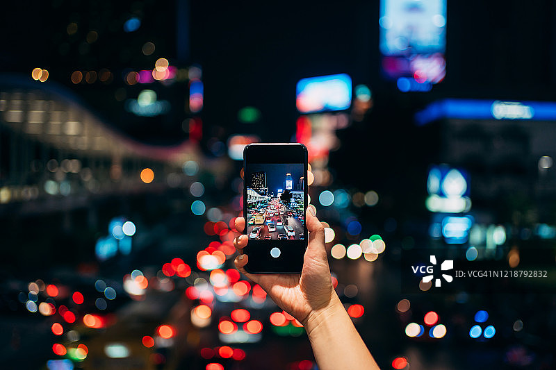 女子在繁华市区用手机拍摄城市高楼和霓虹灯图片素材