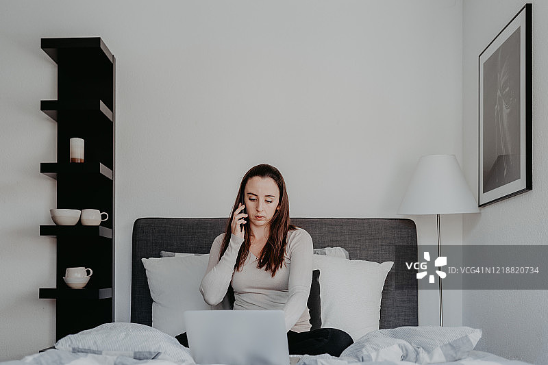 在家办公的女人在床上用智能手机通话图片素材
