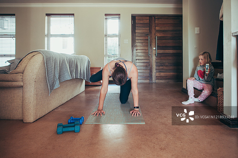 居家普拉提课程，女孩拿着手机和朋友一起练习图片素材