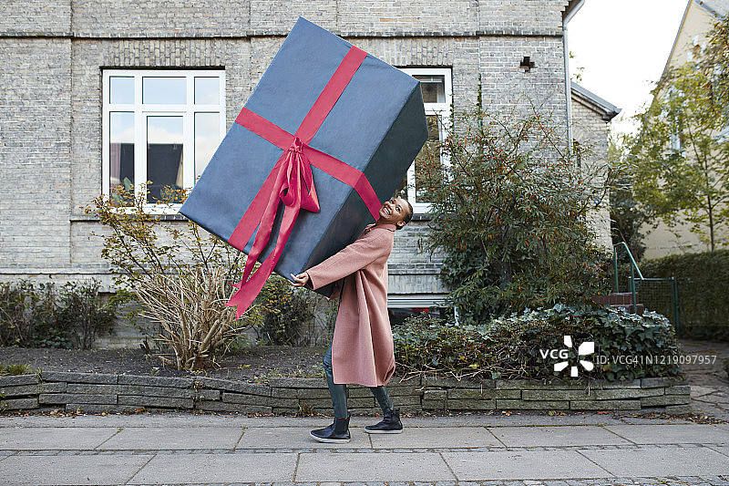 微笑的女人在人行道上抱着一个大礼盒图片素材