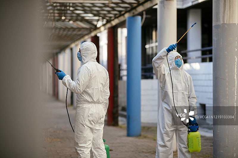 身穿防护服的男子对建筑物入口进行消毒图片素材