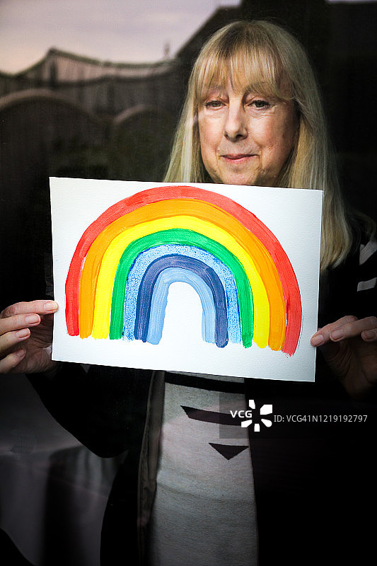 年长女性在窗户上手持彩虹画，支持国家医疗服务图片素材