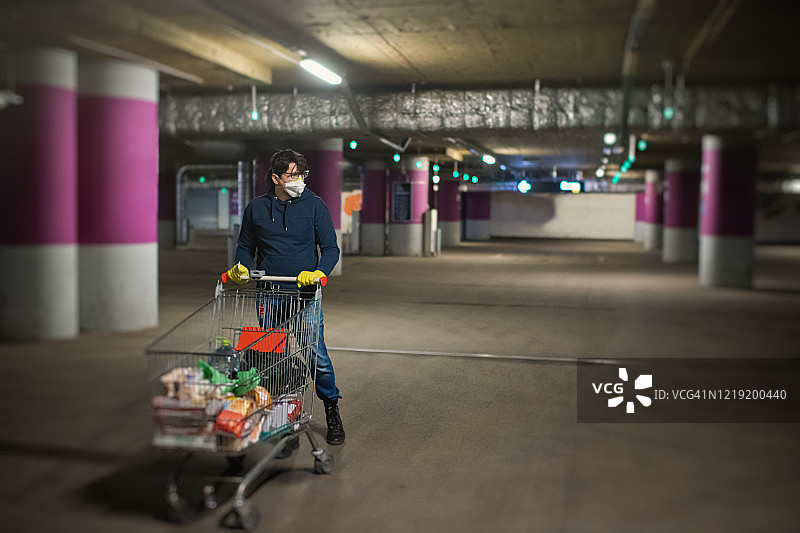 戴口罩橡胶手套的男人，购物后走在空停车场图片素材