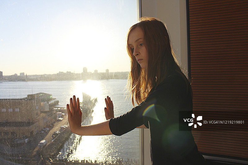 红发少女站在现代卧室落地窗前，眺望哈德逊河和纽约市中心图片素材