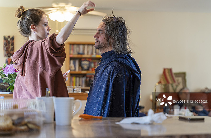 自己动手 - 家庭理发。一个十几岁的女儿给她的父亲，一个50岁留长发的中年男人理发。图片素材