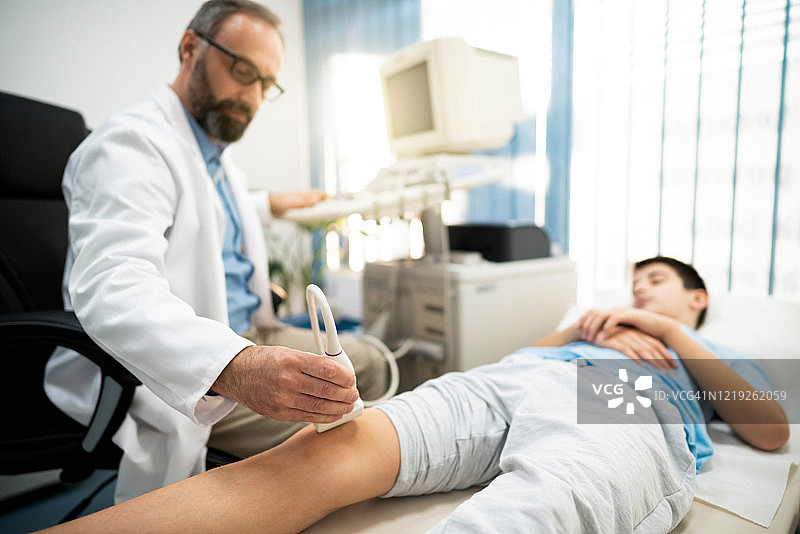 医生使用超声波诊断男孩的膝盖状况图片素材