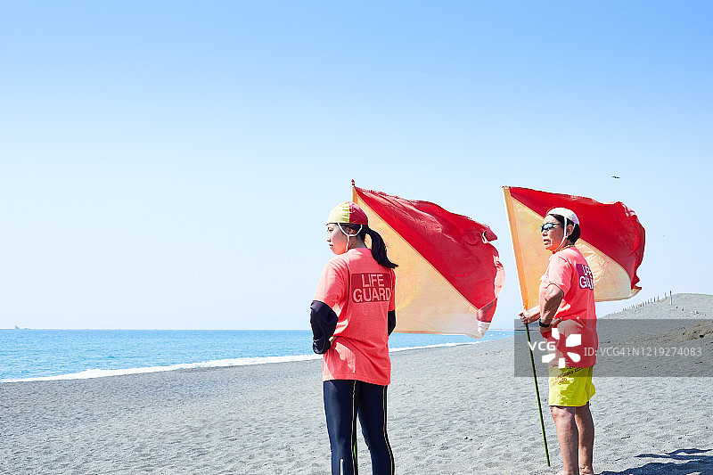 救生员导师和大学生在海边持旗眺望图片素材