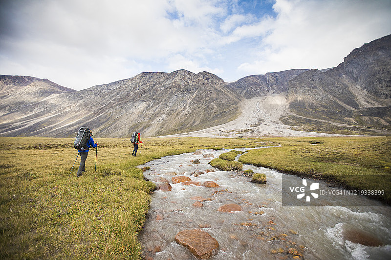 两位背包客在河的上游徒步寻找安全的过河点图片素材