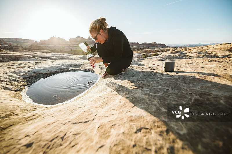 女露营者从浅水坑里取水做饭图片素材