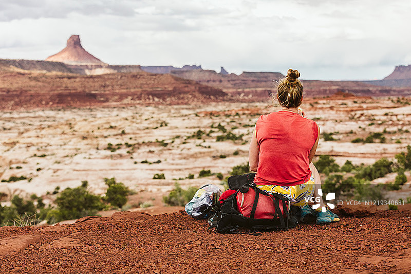 在沙漠景观徒步休息时坐在背包上的出汗女性图片素材