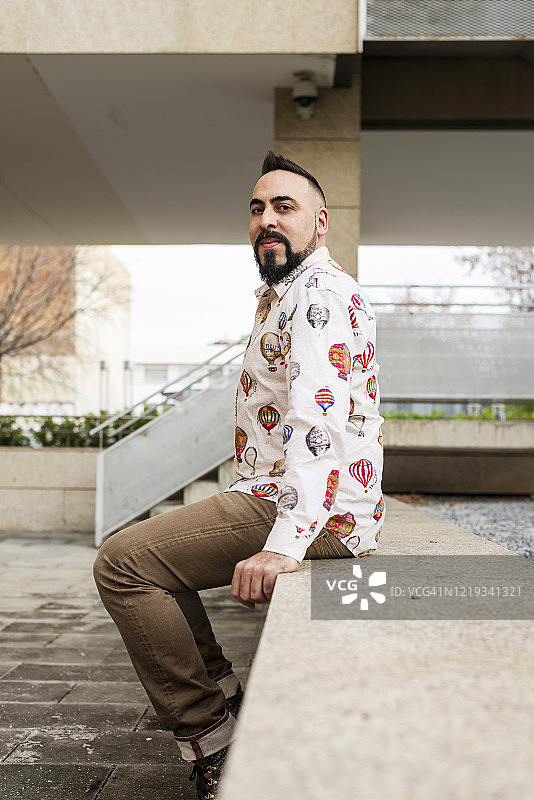 坐在墙上看着镜头的戴珠饰的男人肖像图片素材