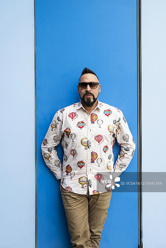 留着胡须的男子戴着太阳镜靠在彩色墙壁上，看着镜头图片素材