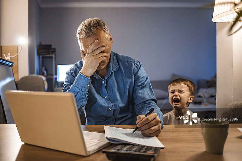 在家工作的压力大男人和两岁儿子图片素材