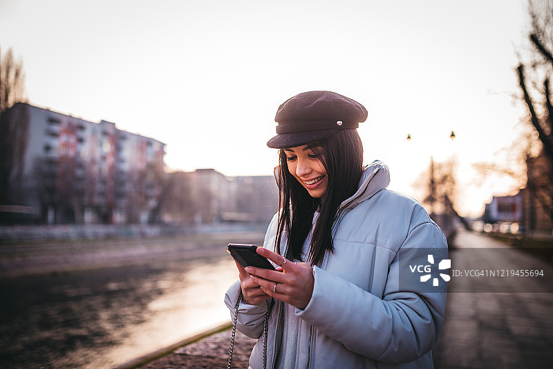 微笑女孩在河边走路并使用手机图片素材