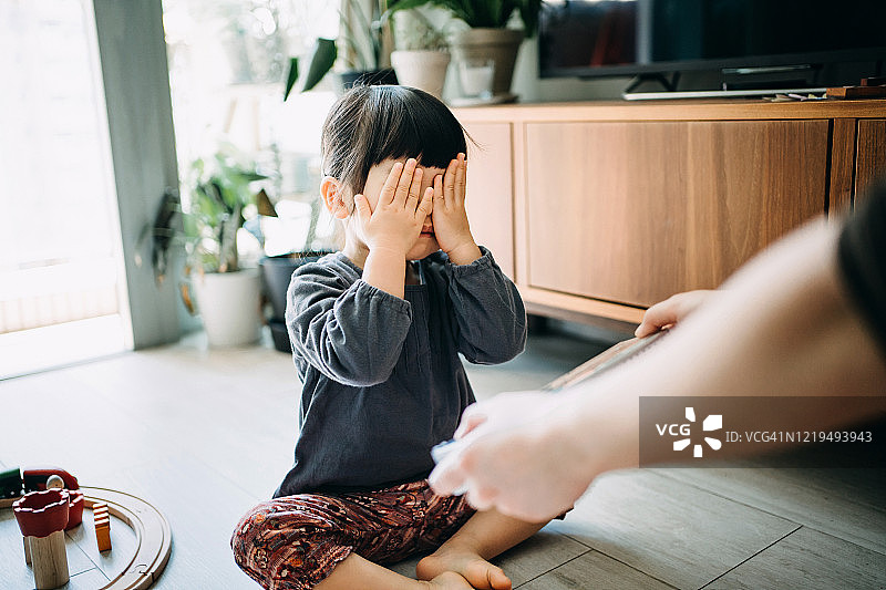在客厅里用双手捂住眼睛，等待礼物惊喜的可爱亚洲小女孩图片素材