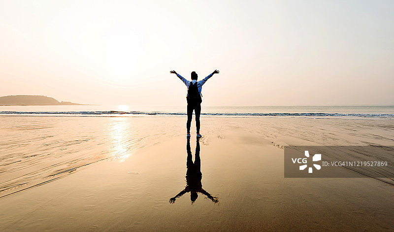 女背包客站在海滩上，举起双臂图片素材