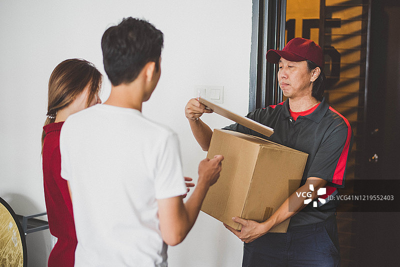 亚洲快递员向微笑的年轻夫妇送货图片素材