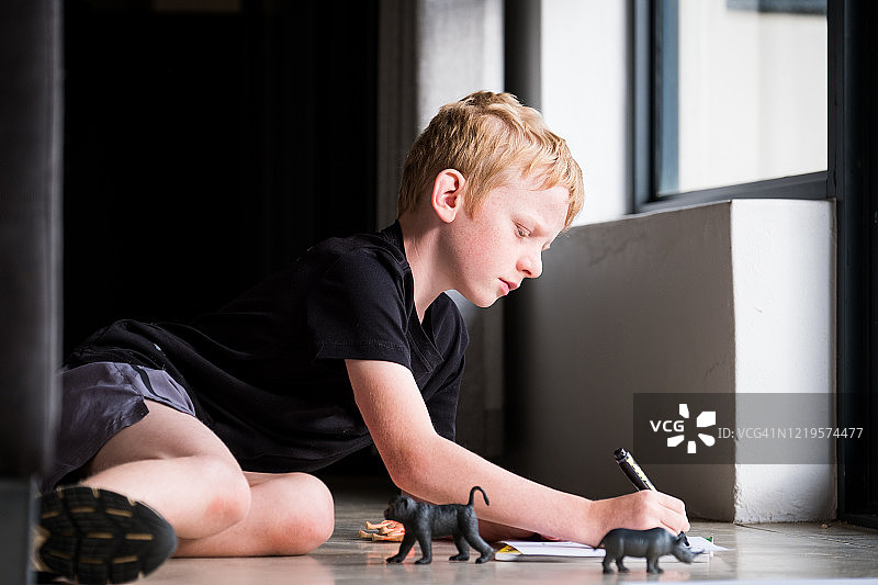 小男孩坐在窗边在纸上画画图片素材