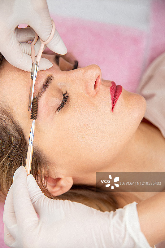 美容师用剪刀和眉梳修剪女士的眉毛 - 摄影素材图片素材