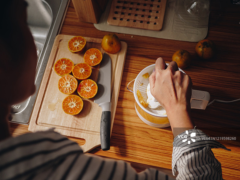 年轻女人在厨房柜台上用榨汁机榨橙汁图片素材