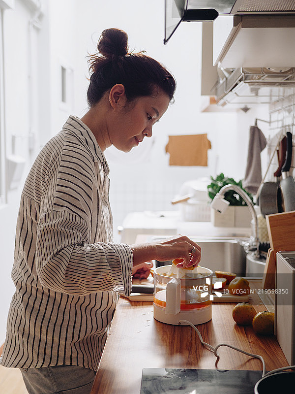 年轻女人在家准备榨橙汁图片素材