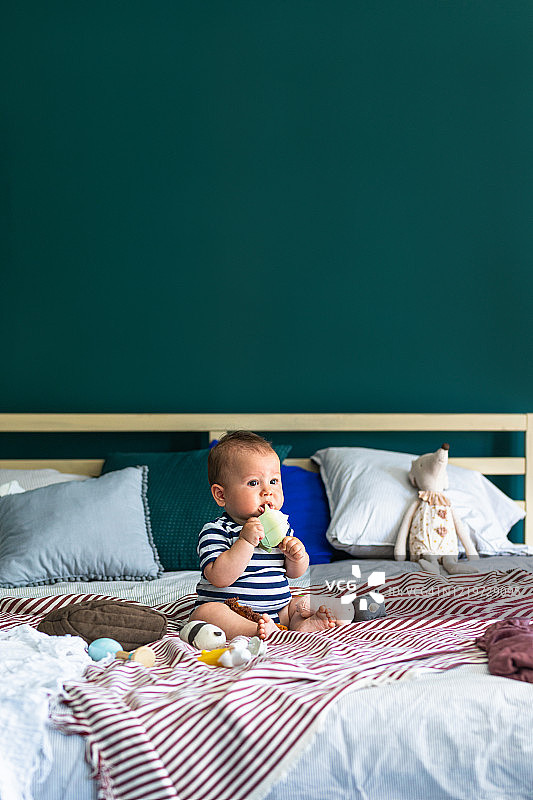 坐在特大号床上咬磨牙器的可爱小男婴图片素材