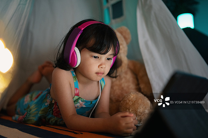 在卧室帐篷里放松，晚上看平板电脑的年轻女孩图片素材